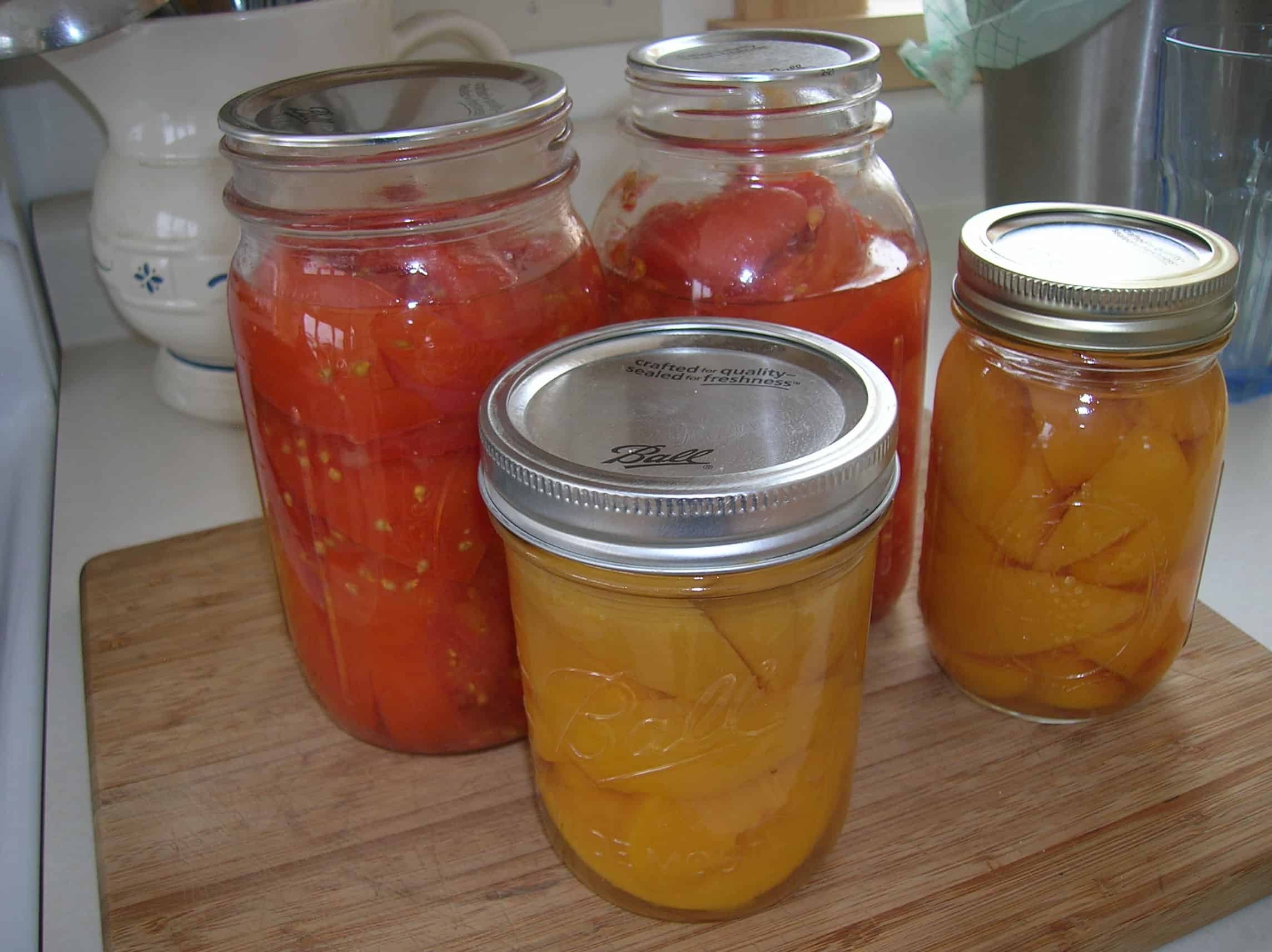 Jars of canned peaches and tomatoes on table